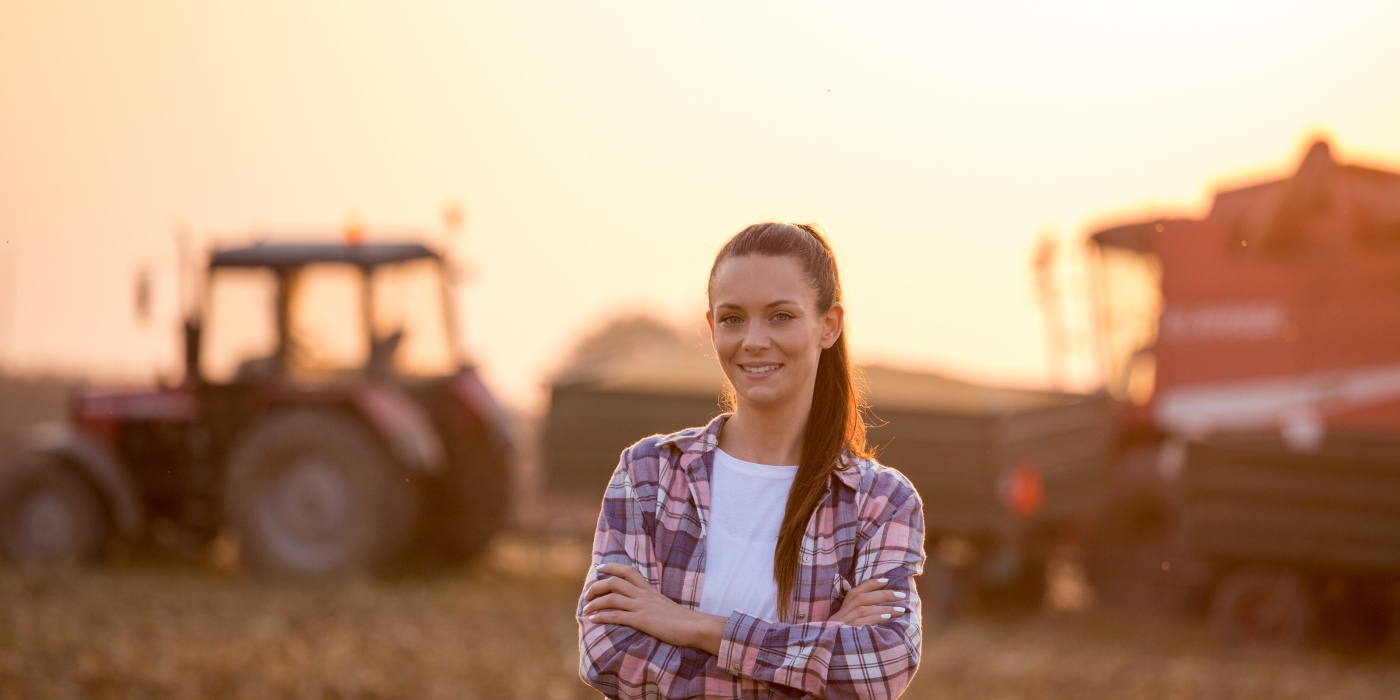 Frau in kariertem Hemd blickt in die Kamera und steht vor einem Traktor